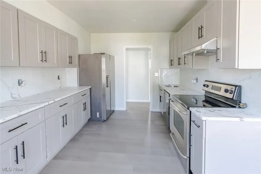 Kitchen with decorative backsplash, appliances with stainless steel finishes, under cabinet range hood, and light stone countertops
