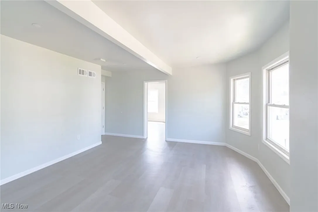 Empty room featuring wood finished floors and beamed ceiling