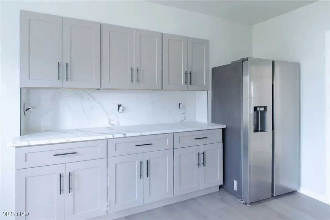Kitchen featuring stainless steel refrigerator with ice dispenser, light stone countertops, tasteful backsplash, gray cabinets, and light wood finished floors