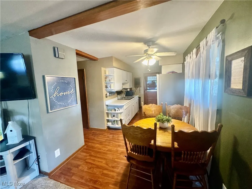 Dining area featuring light wood-style flooring, beamed ceiling, and a ceiling fan