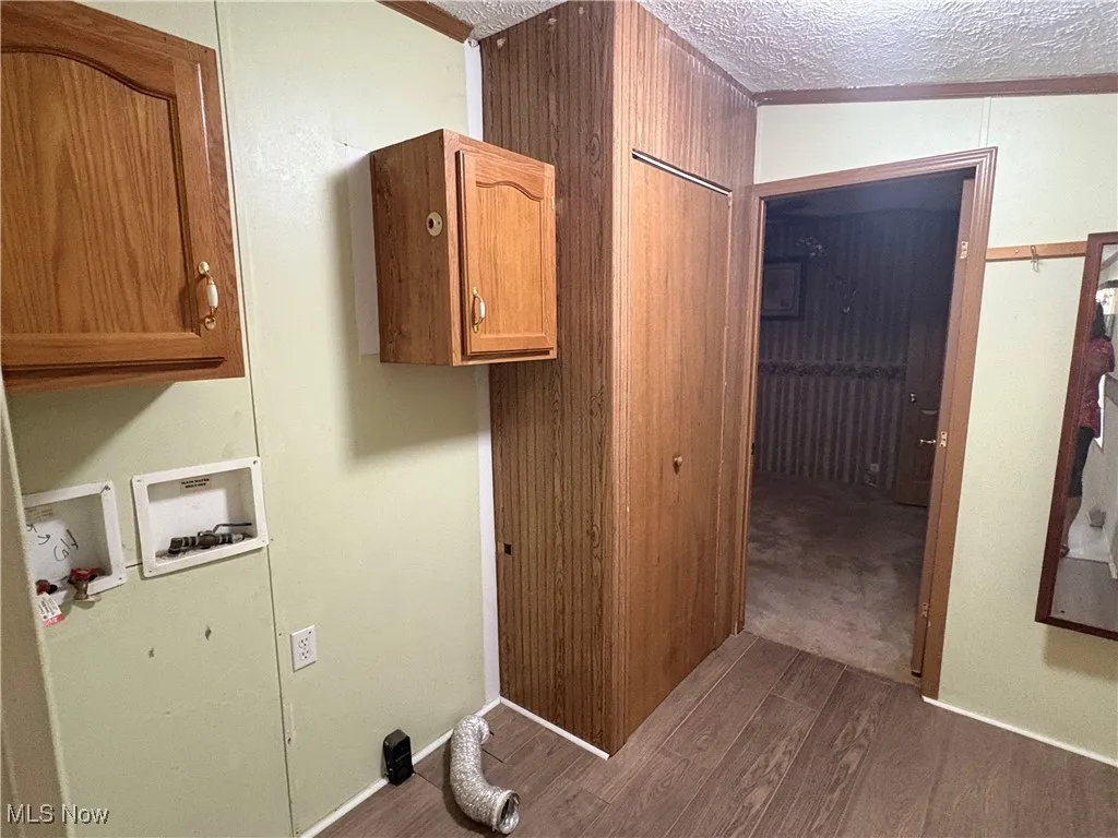 Washroom featuring dark wood finished floors, a textured ceiling, hookup for a washing machine, cabinet space, and wood walls