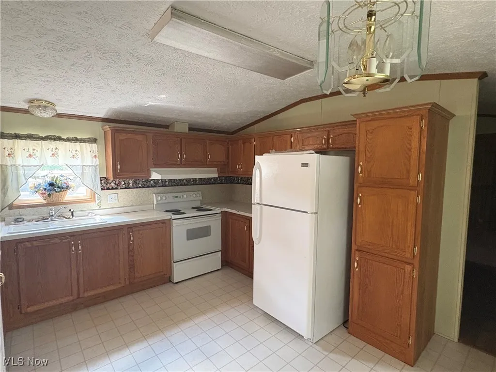 Kitchen with a textured ceiling, white appliances, light countertops, brown cabinetry, and ornamental molding