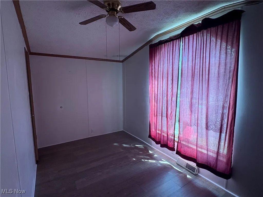 Spare room featuring a textured ceiling, dark wood-type flooring, ornamental molding, and a ceiling fan