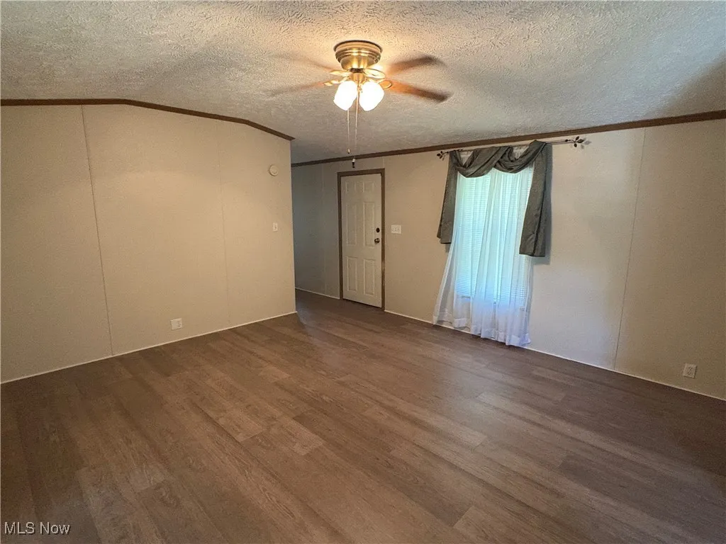 Empty room featuring crown molding, wood finished floors, ceiling fan, and a textured ceiling