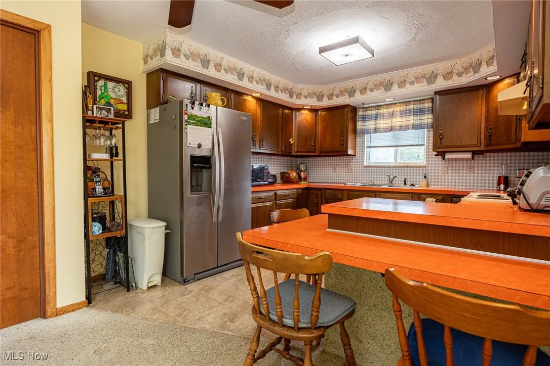 Kitchen featuring stainless steel fridge with ice dispenser, light countertops, decorative backsplash, a textured ceiling, and a kitchen breakfast bar
