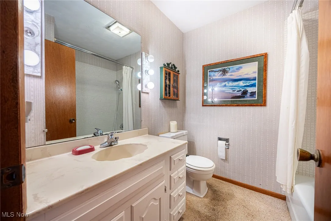 Full bath with wallpapered walls, vanity, and shower / tub combo with curtain