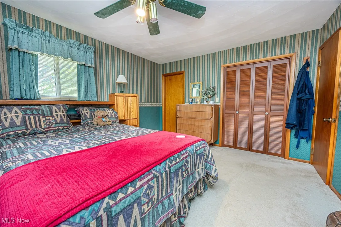 Carpeted bedroom with a closet, ceiling fan, and wallpapered walls