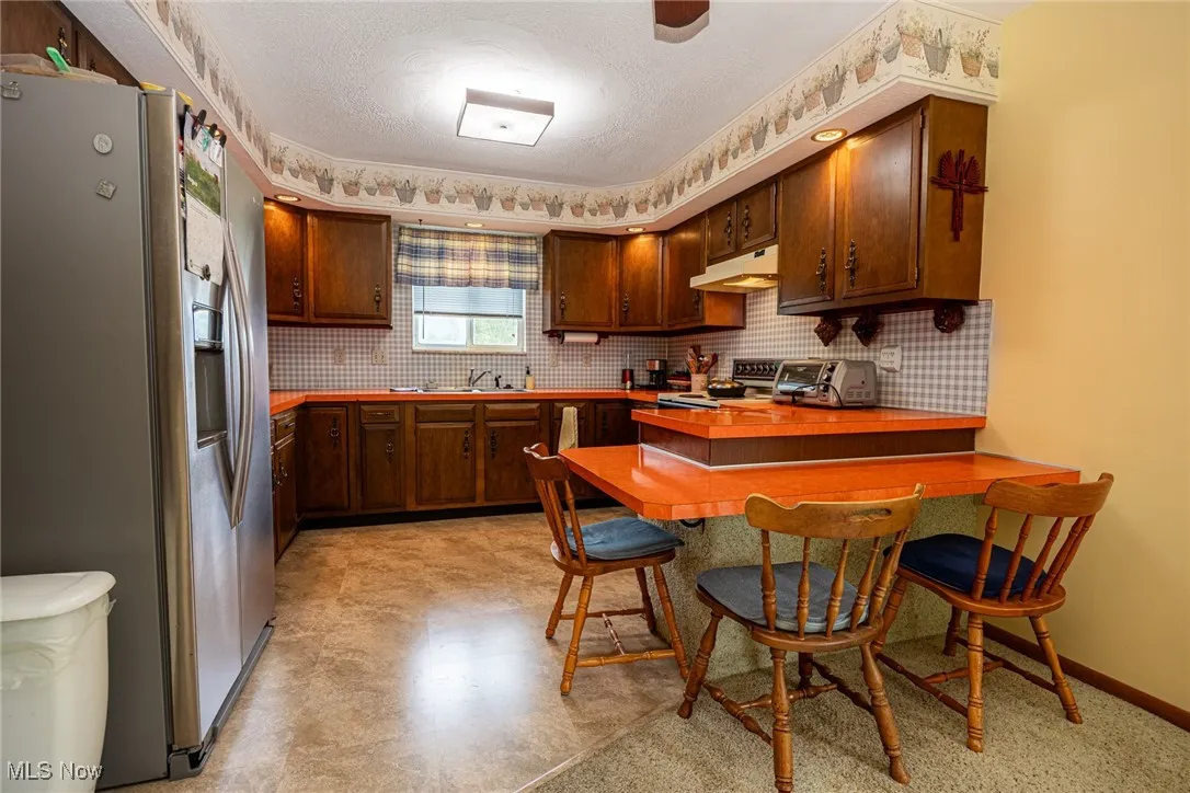 Kitchen featuring stainless steel appliances, a peninsula, backsplash, a kitchen bar, and a textured ceiling