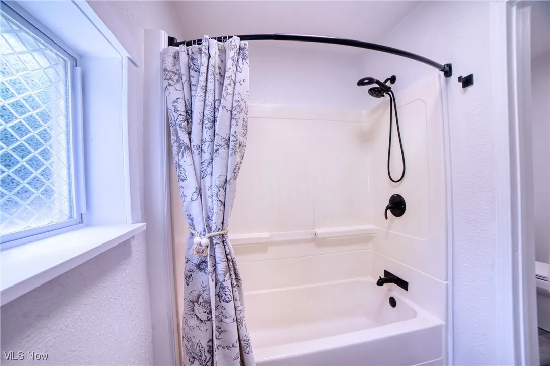 Full bath with a textured wall, shower / bath combo, and plenty of natural light