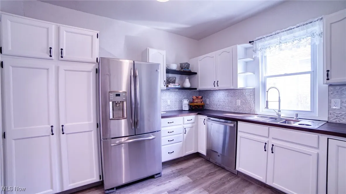 Kitchen featuring open shelves, stainless steel appliances, white cabinetry, light wood-style flooring, and decorative backsplash