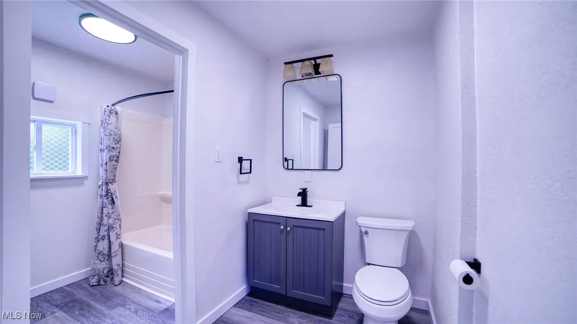 Bathroom with shower / tub combo with curtain, dark wood-style flooring, and vanity