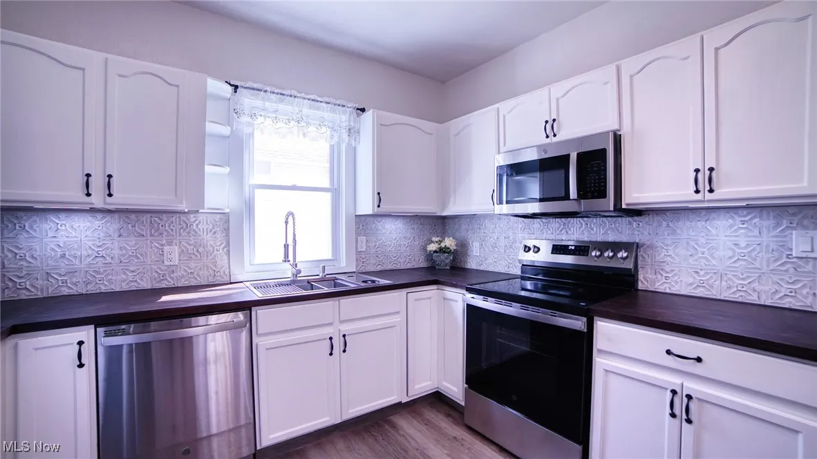 Kitchen featuring stainless steel appliances, white cabinets, and tasteful backsplash