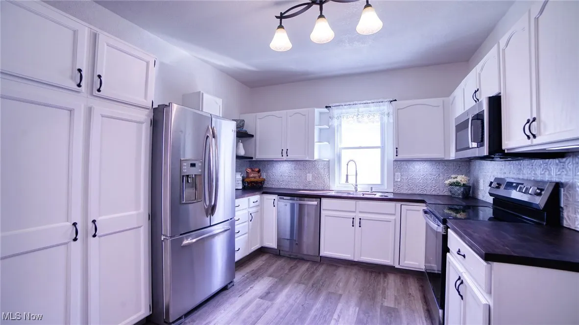 Kitchen with stainless steel appliances, open shelves, white cabinets, dark wood finished floors, and backsplash