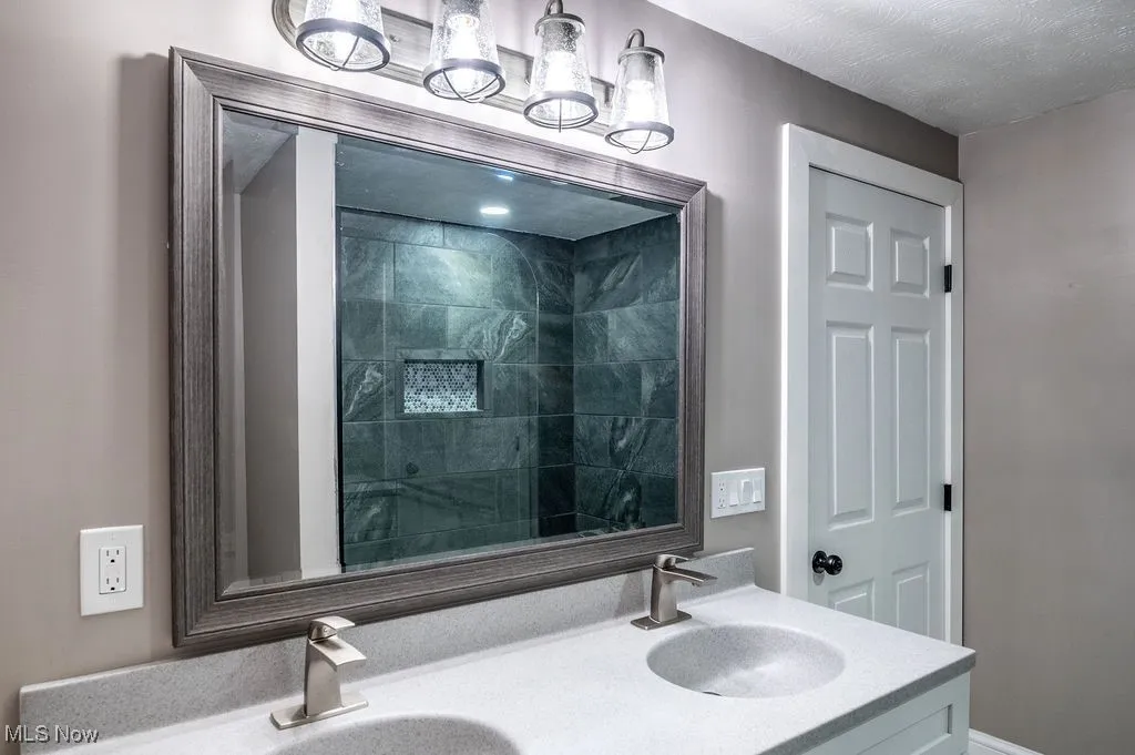 Full bath with double vanity, a tile shower, and a textured ceiling