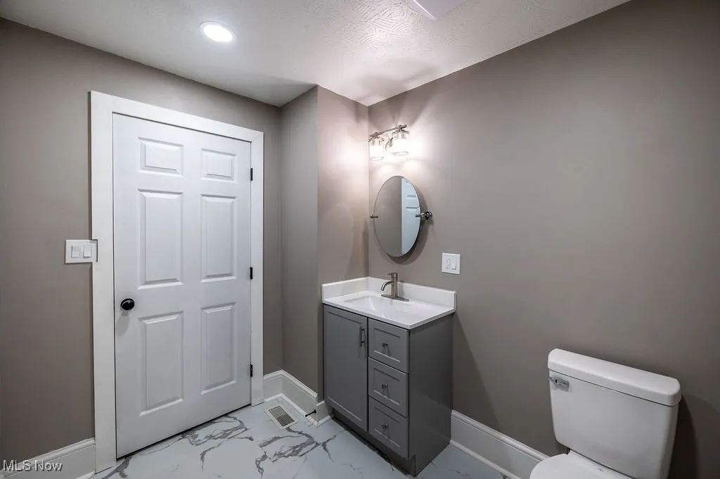 Half bath featuring light marble finish floors, vanity, and recessed lighting