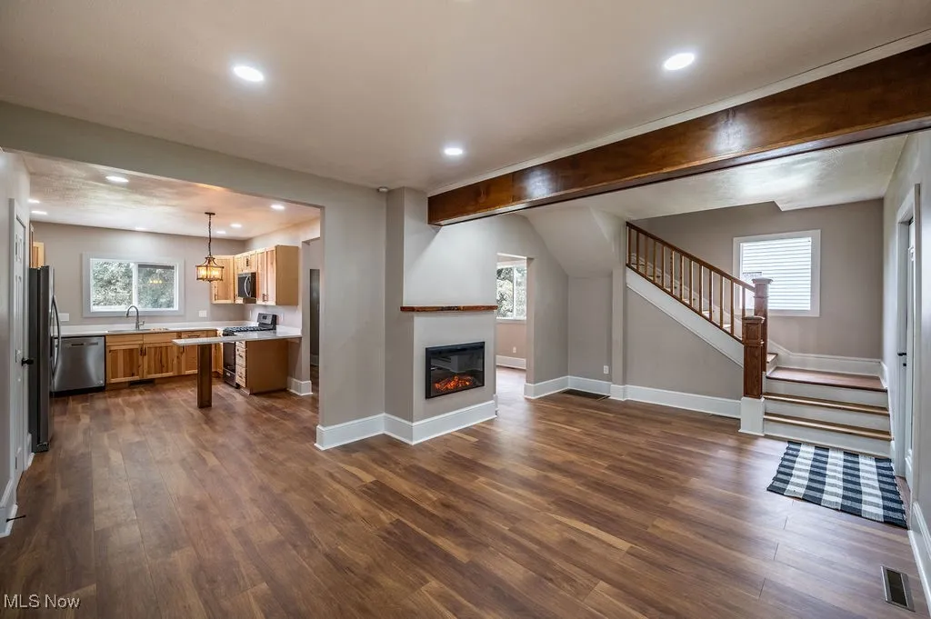 Unfurnished living room featuring stairs, a glass covered fireplace, healthy amount of natural light, dark wood-type flooring, and recessed lighting