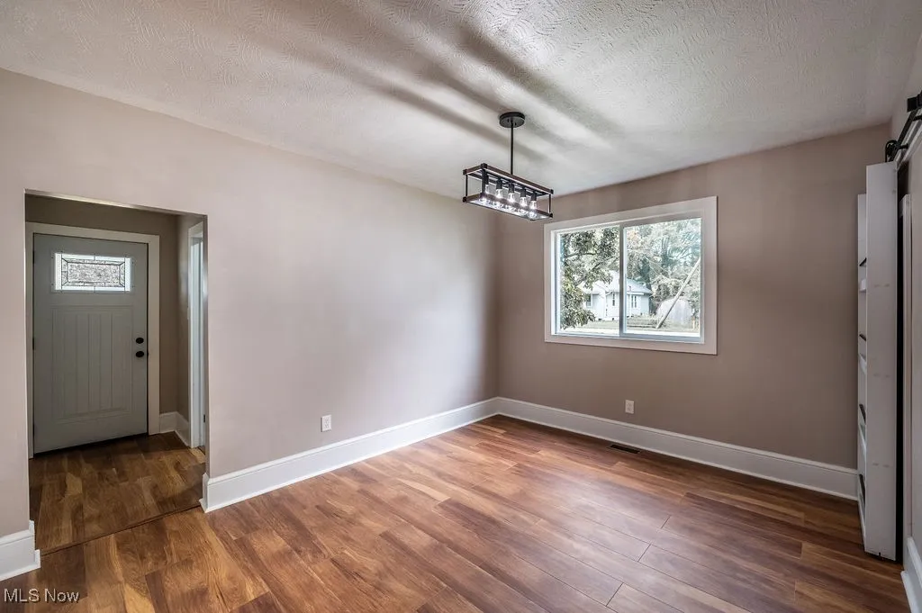Unfurnished dining area featuring a textured ceiling, plenty of natural light, dark wood-style flooring, and a barn door