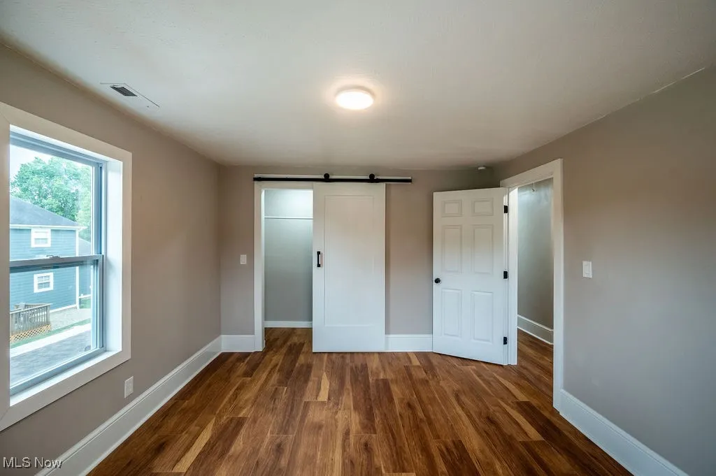 Unfurnished bedroom featuring a barn door and dark wood finished floors