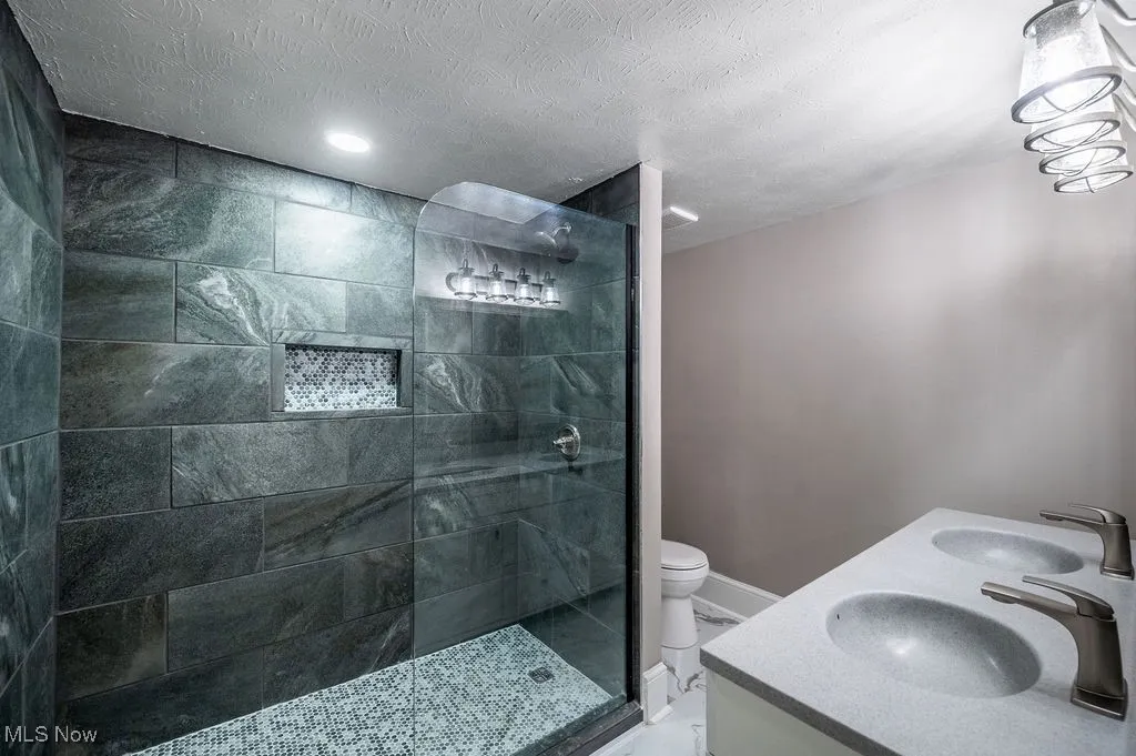 Full bath featuring walk in shower, double vanity, and a textured ceiling
