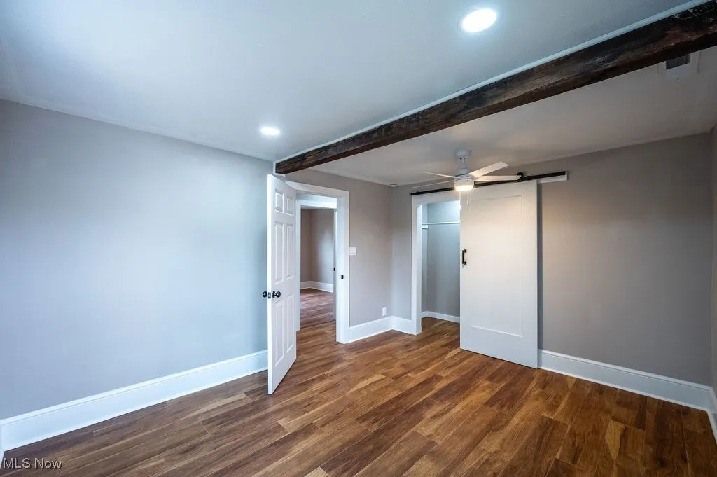 Spare room featuring a barn door, dark wood-style flooring, a ceiling fan, recessed lighting, and beam ceiling