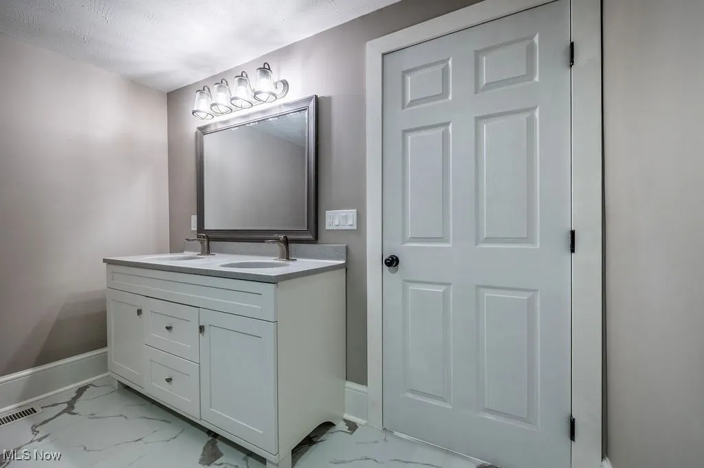 Full bath with light marble finish floors and double vanity
