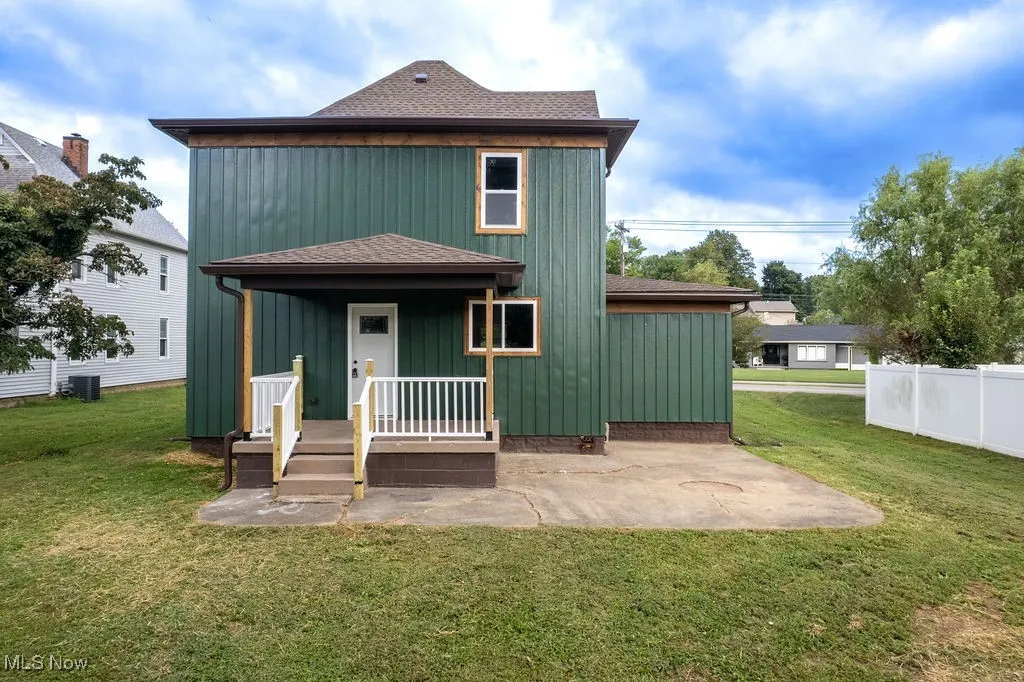 Back of property with roof with shingles, a lawn, board and batten siding, and a patio