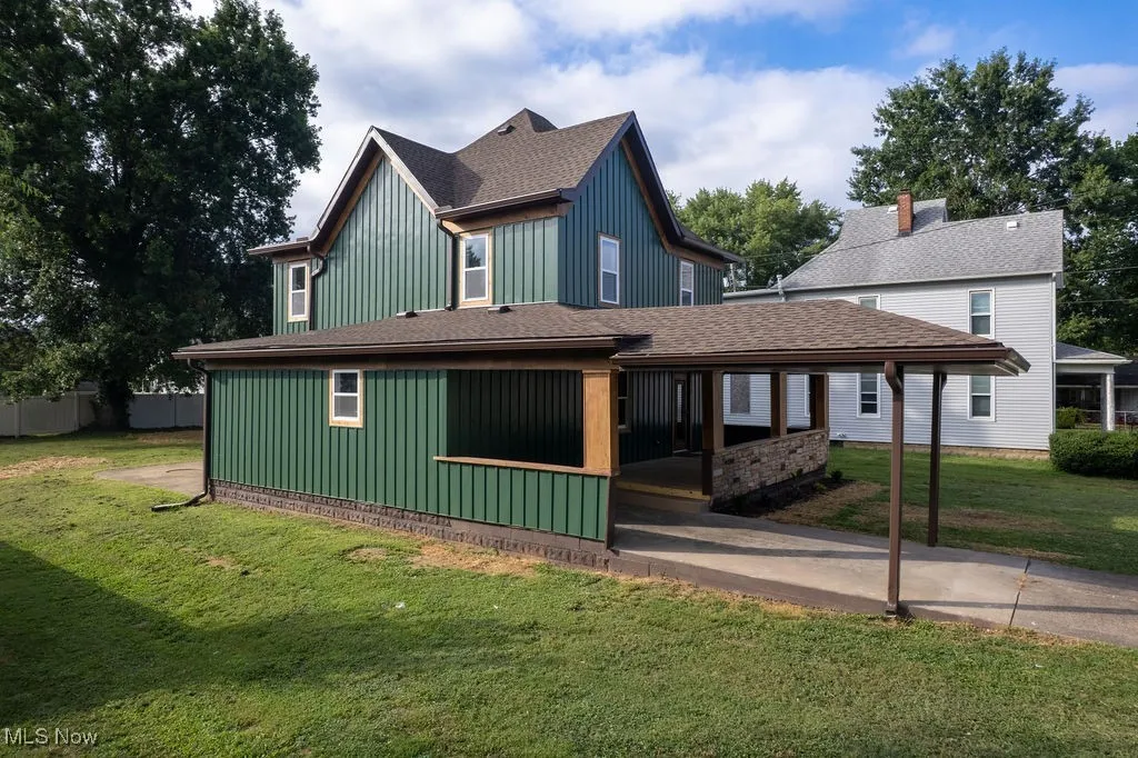 View of front of property with roof with shingles, board and batten siding, a front lawn, a carport, and concrete driveway