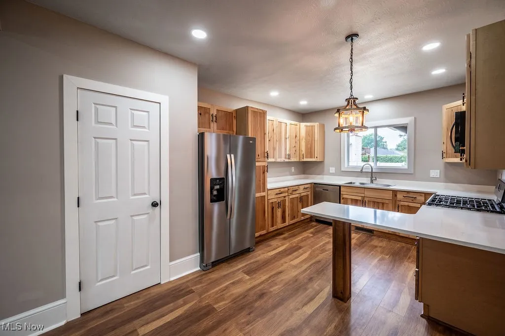 Kitchen with stainless steel appliances, hanging light fixtures, dark wood-type flooring, recessed lighting, and a peninsula