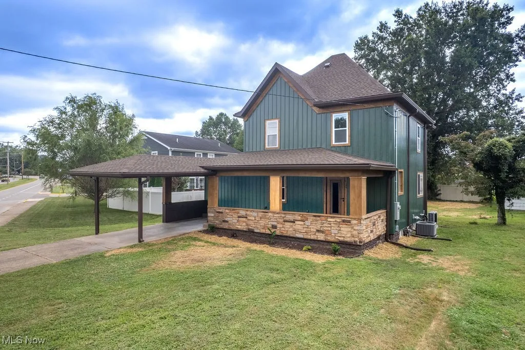 View of front of property featuring an attached carport, roof with shingles, concrete driveway, stone siding, and board and batten siding