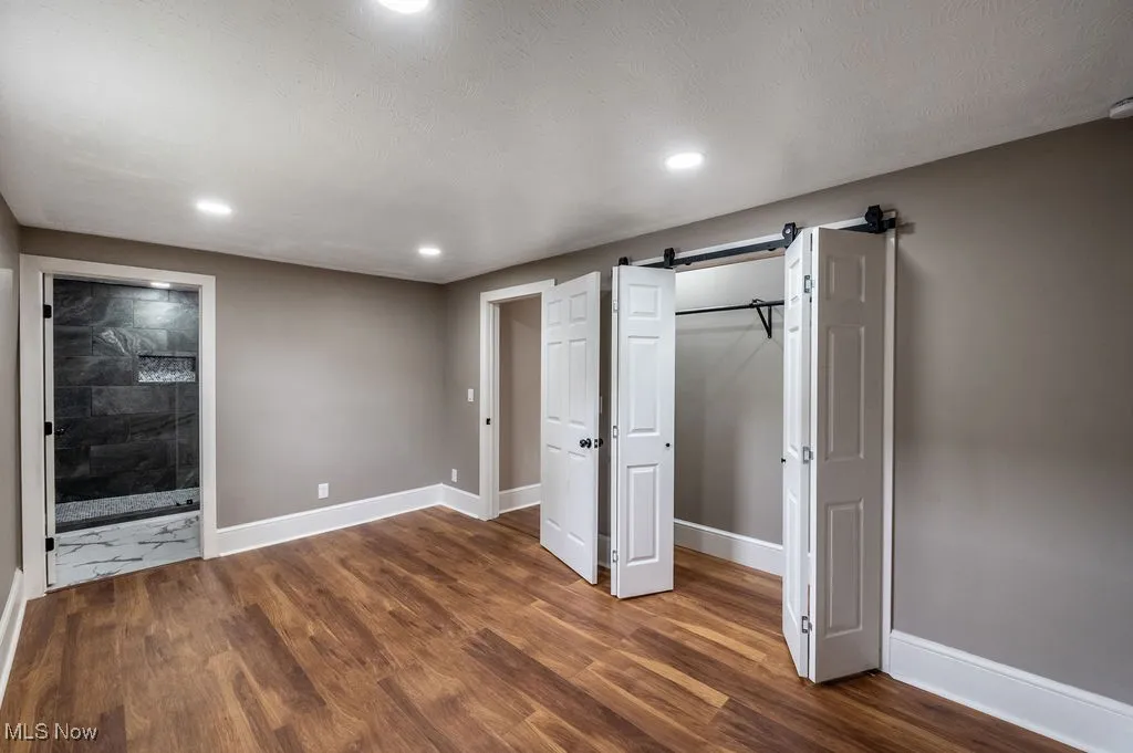 Unfurnished bedroom with a barn door, recessed lighting, dark wood-style floors, connected bathroom, and a textured ceiling