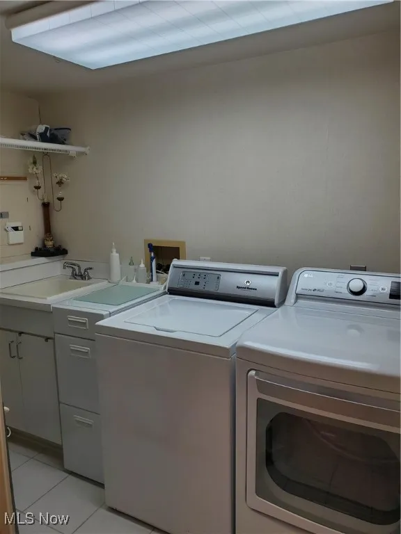 Washroom with light tile patterned floors, washer and dryer, and cabinet space