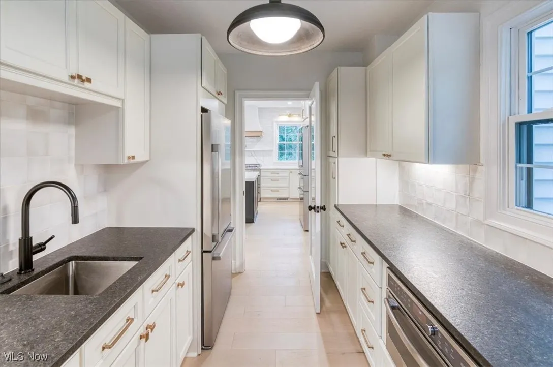 Kitchen with decorative backsplash, stainless steel appliances, white cabinets, and dark stone countertops