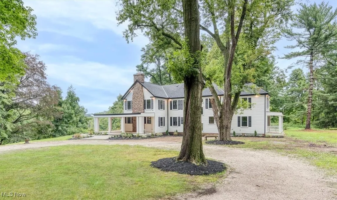 Colonial-style house featuring a porch, curved driveway, a front yard, a chimney, and view of wooded area