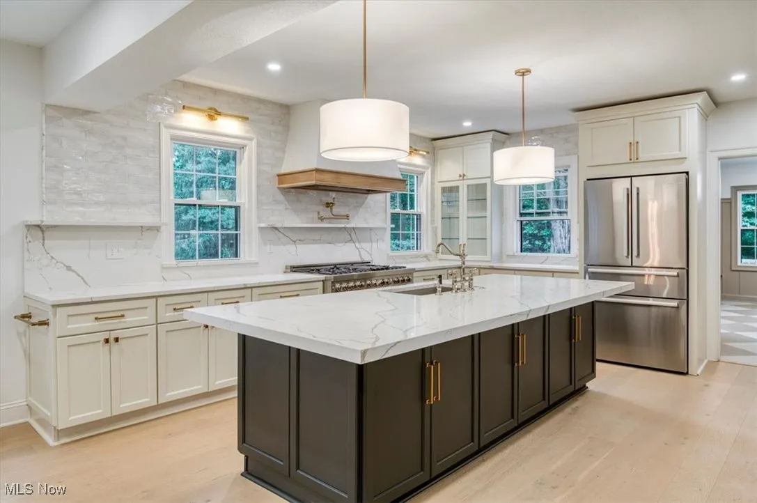 Kitchen with light stone counters, light wood finished floors, decorative backsplash, stainless steel refrigerator, and pendant lighting
