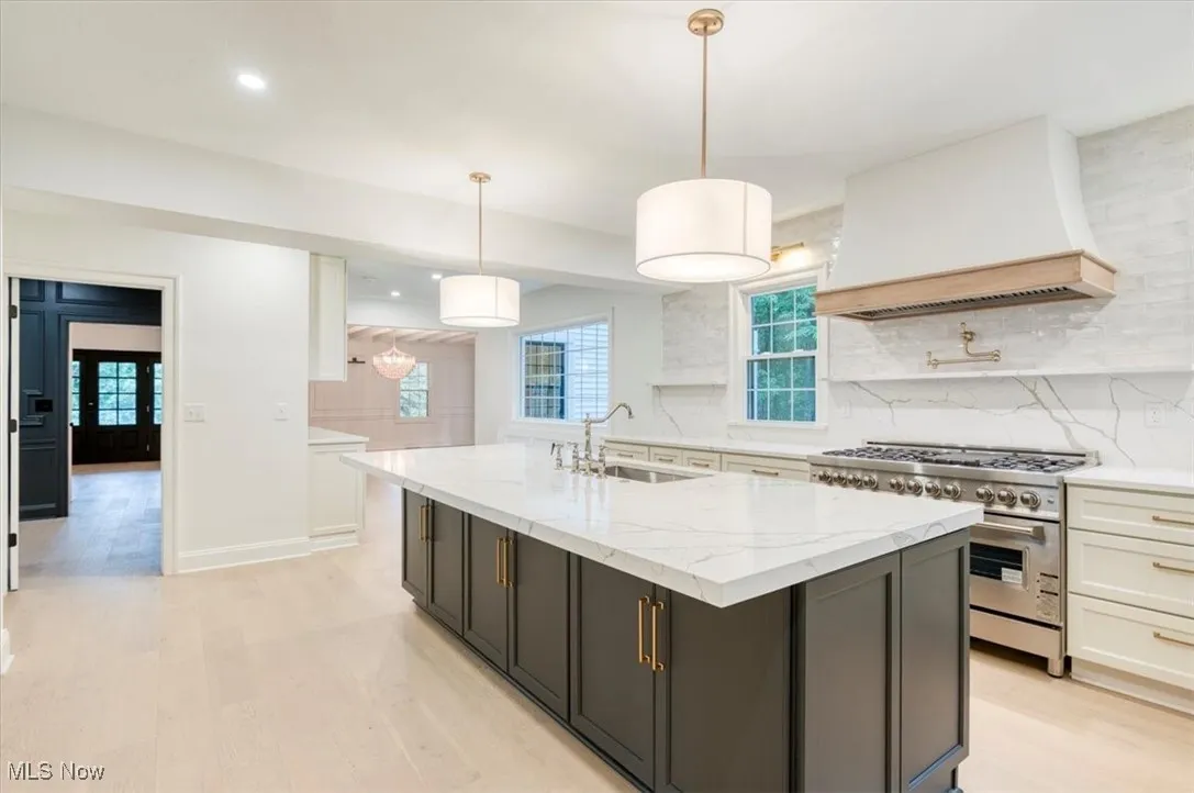 Kitchen featuring high end stainless steel range oven, backsplash, light stone counters, premium range hood, and recessed lighting