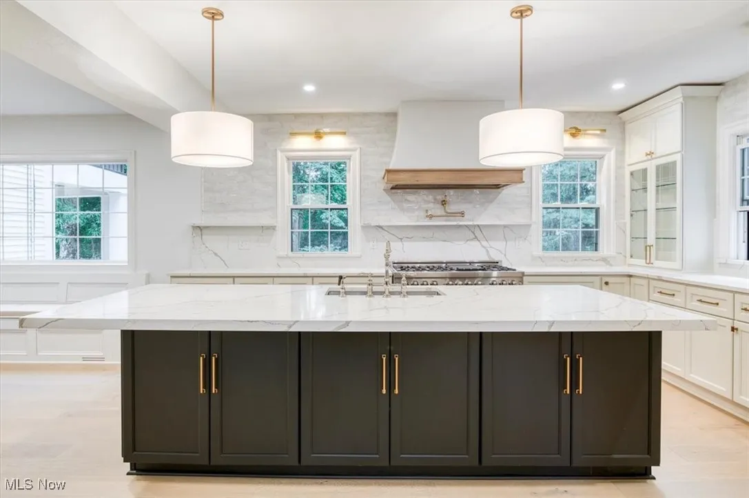 Kitchen with dark cabinetry, decorative backsplash, light stone counters, premium range hood, and recessed lighting