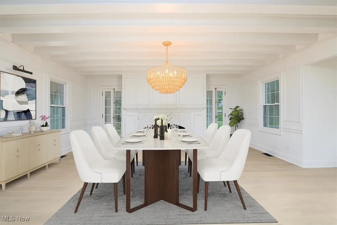 Dining area with light wood finished floors, beamed ceiling, a chandelier, and a decorative wall