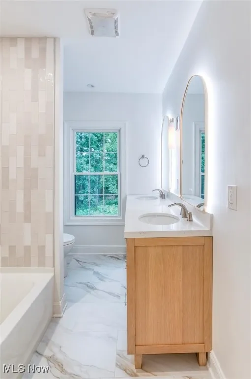Bathroom featuring light marble finish floors, a bath, and double vanity