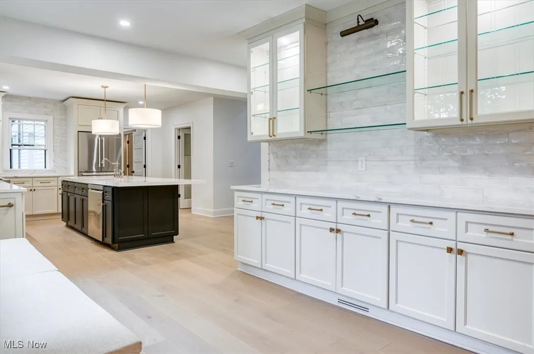 Kitchen featuring hanging light fixtures, white cabinetry, light stone counters, light wood-style flooring, and an island with sink