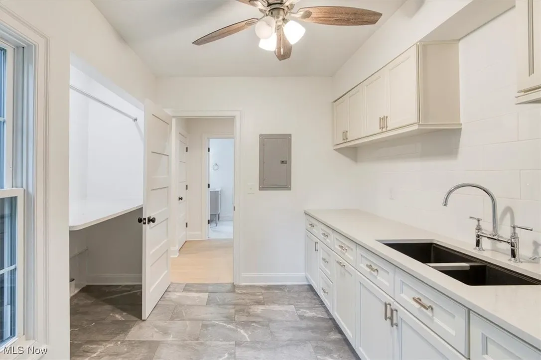 Second floor laundry featuring white cabinets, light stone counters, electric panel, ceiling fan, and decorative backsplash