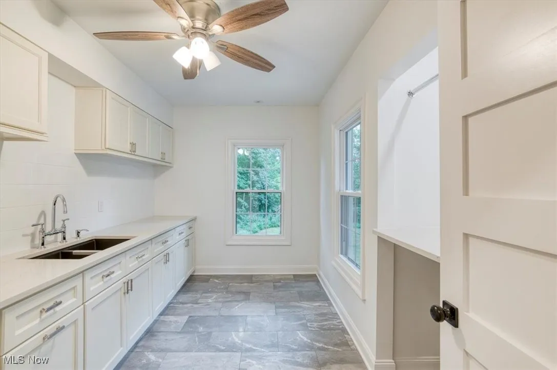 Second floor laundry featuring dark stone finish floors, white cabinets, backsplash, and light stone counters