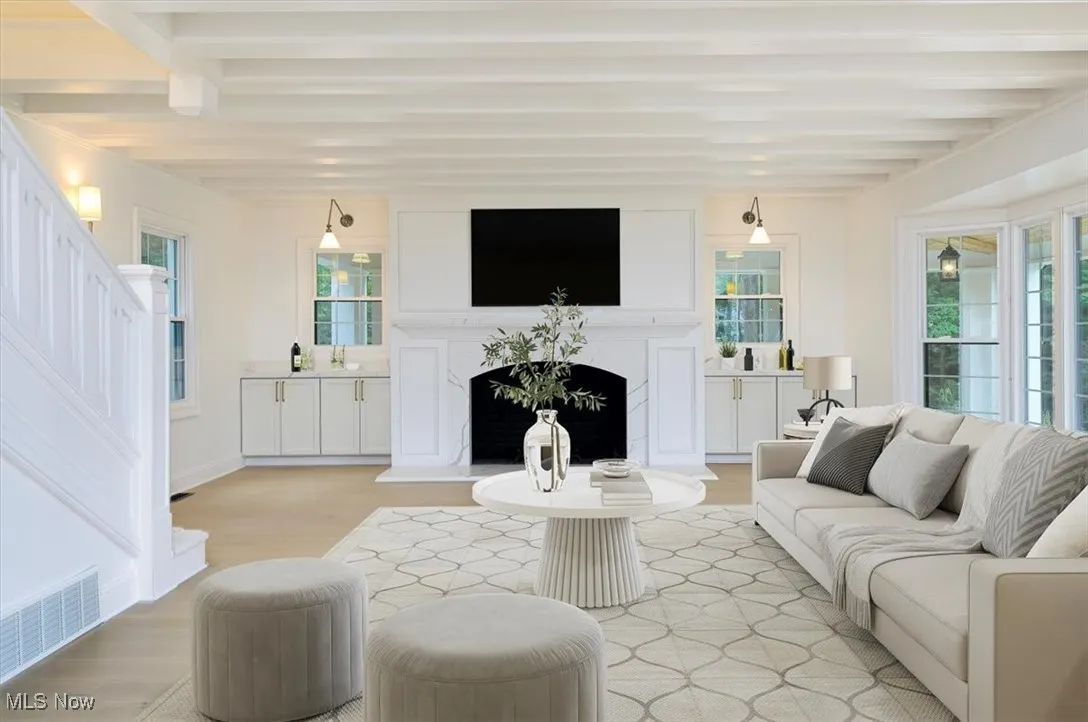 Living room with beamed ceiling, stairs, light wood-type flooring, a fireplace, and healthy amount of natural light