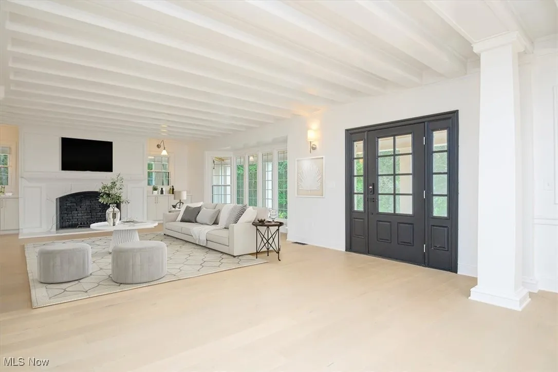 Living room featuring beam ceiling, light wood-style flooring, decorative columns, and a fireplace