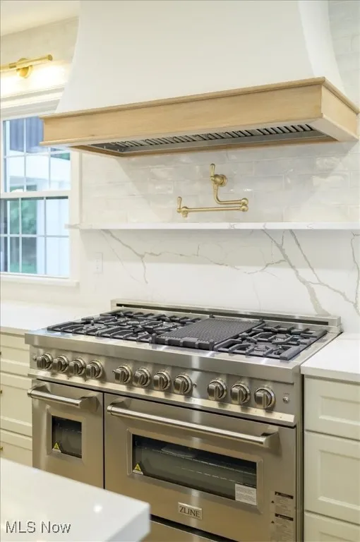 Kitchen with premium range hood, backsplash, double oven range, white cabinetry, and light stone countertops
