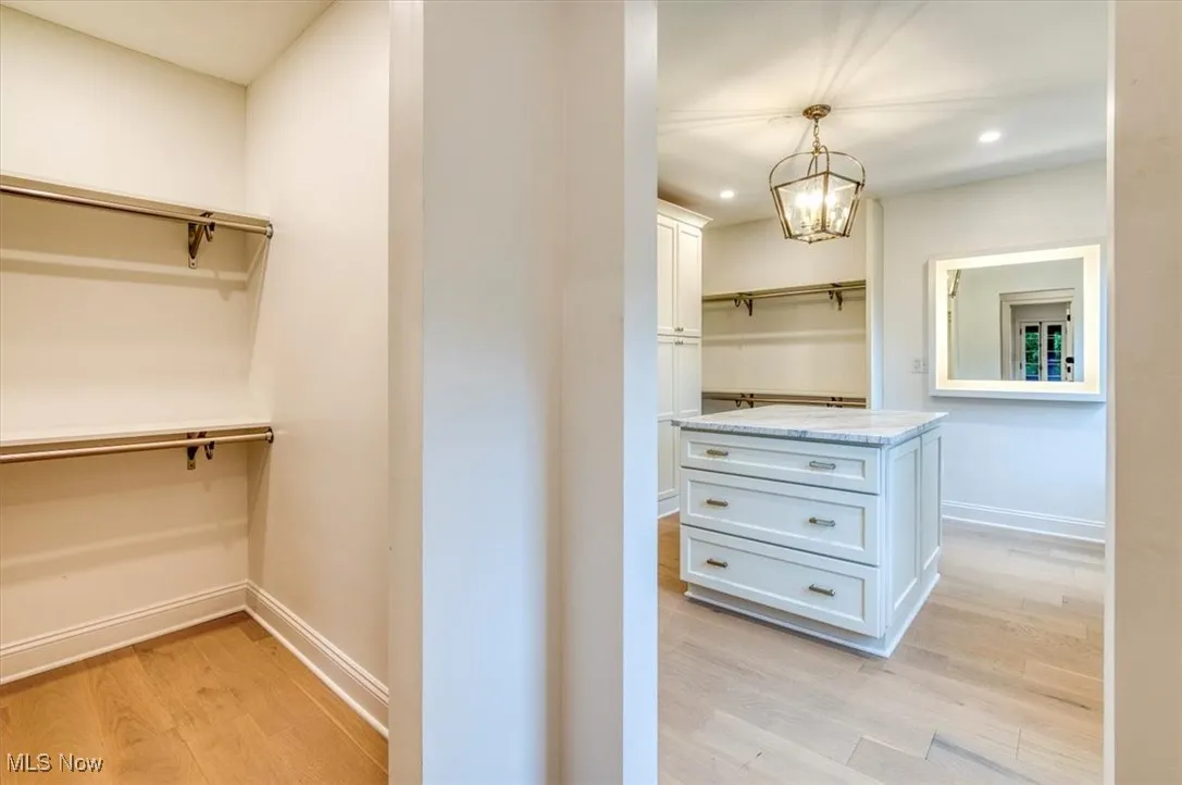 Spacious closet with light wood-type flooring and a chandelier