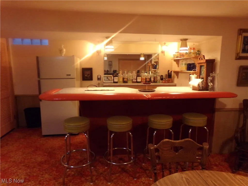 Indoor wet bar featuring freestanding refrigerator, light countertops, and dark carpet