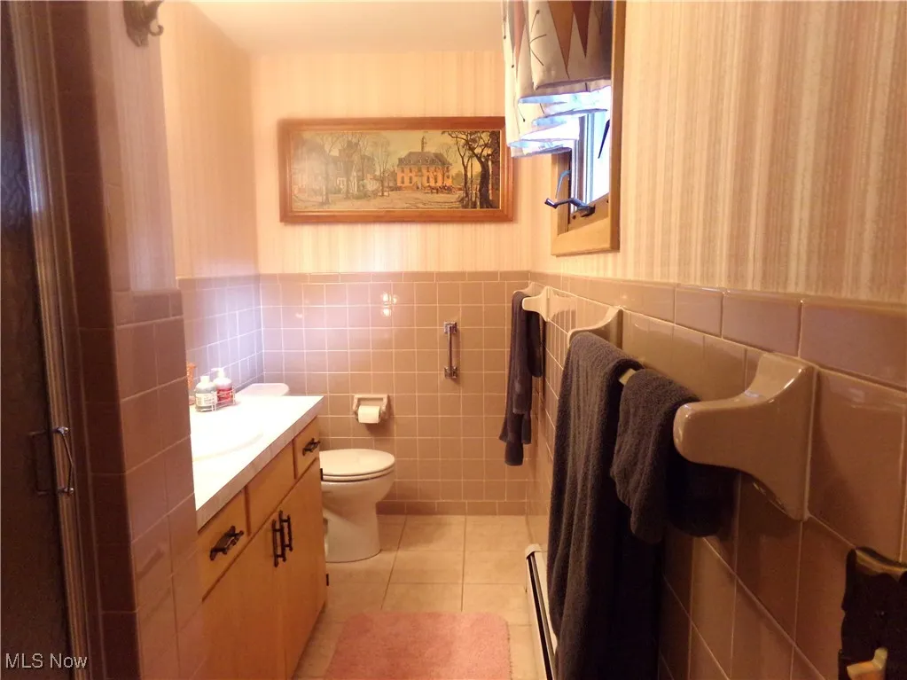 Full bath with wallpapered walls, light tile patterned floors, tile walls, wainscoting, and vanity