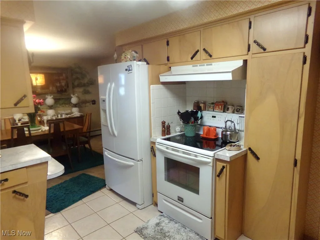 Kitchen featuring white appliances, under cabinet range hood, light tile patterned floors, and light countertops