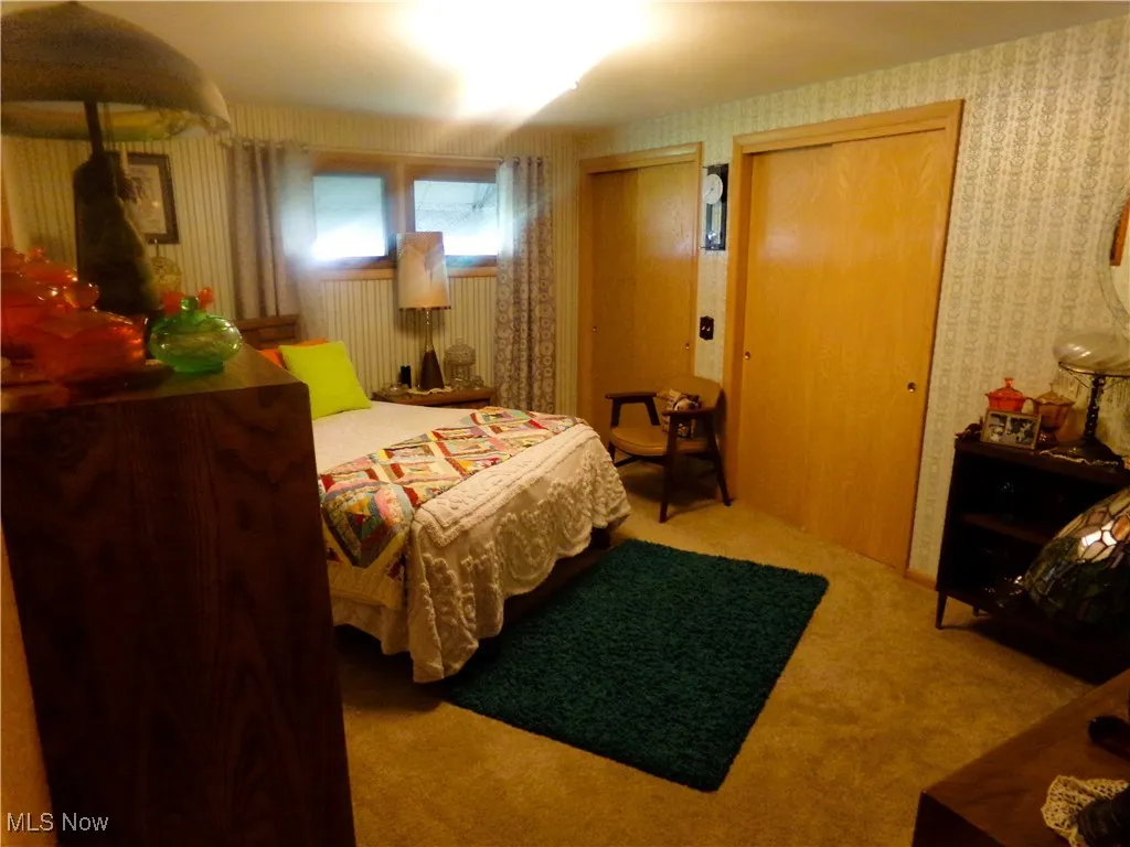 Bedroom featuring carpet, two closets, and wallpapered walls