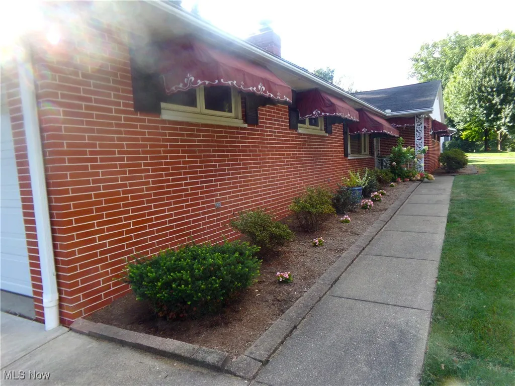 View of property exterior with brick siding, a chimney, and a lawn